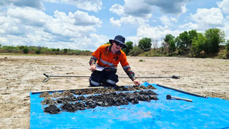 Joshua Crow in PPE kneeling next to tailings samples