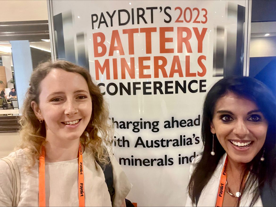 Rosie Blannin and Anita Parbhakar-Fox in front of the Paydirt 2023 Battery Minerals conference poster