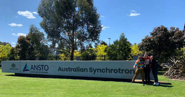 Loren Nicholls and Mayra Jefferson Montoya with Dr Andrew Langendam in front of the Australian Synchrotron sign