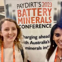 Rosie Blannin and Anita Parbhakar-Fox in front of the Paydirt 2023 Battery Minerals conference poster
