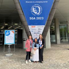 Rosie Blannin, Olivia Mejías, and Loren Nichols in front of  Society for Geology Applied to Mineral Deposits (SGA) banner