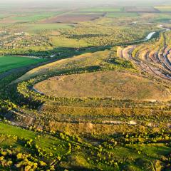 Aerial shot of green landscape and open pit at sunset